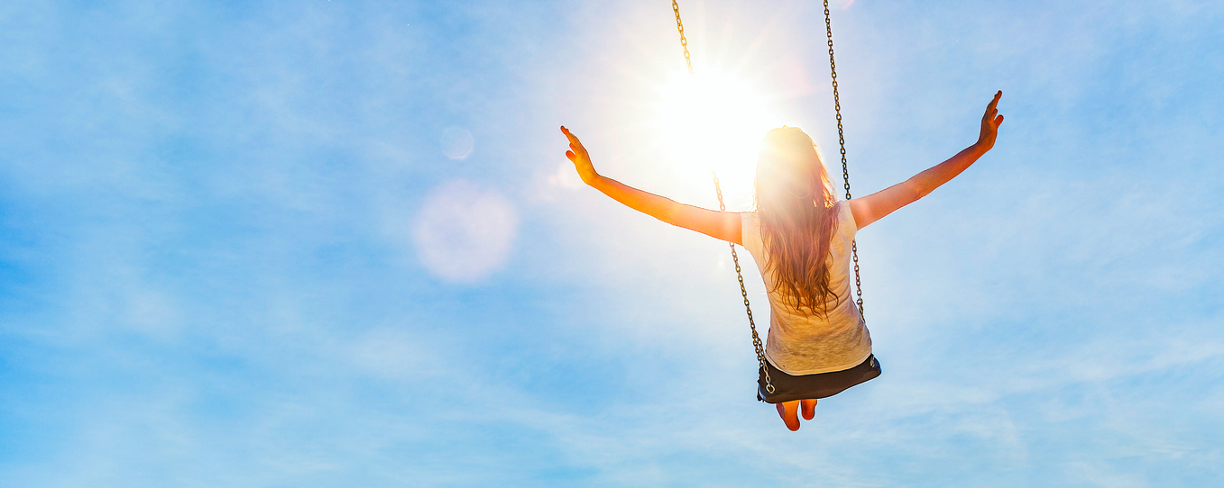 Beautiful bright sky, person on a swing facing the sun shining on their face.